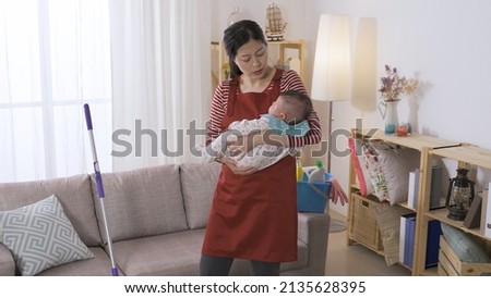 Japanese housewife busy with house chores is getting her young daughter to nap by patting her softly at a bright home interior. Royalty-Free Stock Photo #2135628395