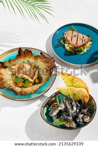 Fish dishes on white background in minimal concept menu. Set from mussels, halibut and tuna in ceramic plate with hard shadows. Mediterranean set with fish and seafood. Modern cuisine Royalty-Free Stock Photo #2135629339
