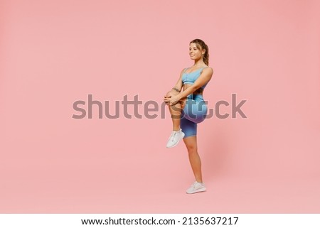 Full size young sporty athletic fitness trainer woman wear blue tracksuit spend time in home gym train do stretch legs exercise isolated on pastel plain light pink background. Workout sport concept