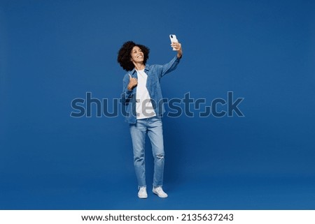 Full body young smiling black woman in casual clothes shirt white t-shirt doing selfie shot on mobile cell phone post photo on social network isolated on plain dark blue background studio portrait.