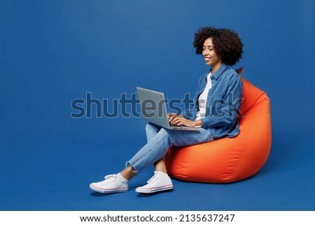Full body young smiling student fun happy black woman in casual clothes shirt white t-shirt sit in bag chair hold use work on laptop pc computer isolated on plain dark blue background studio portrait. Royalty-Free Stock Photo #2135637247