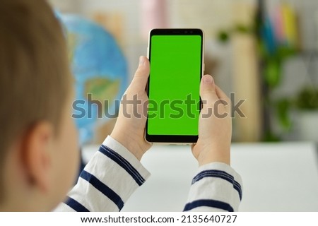 The child is holding a phone in his hand with a green screen.