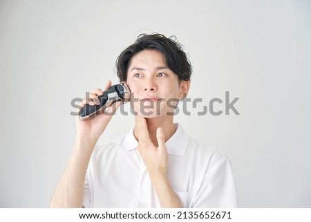 Asian man shaving with electric shaver Royalty-Free Stock Photo #2135652671