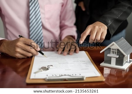 A real estate agent with rental homes and home insurance for clients to sign contracts under a formal home lease agreement. Home rental and insurance concept.