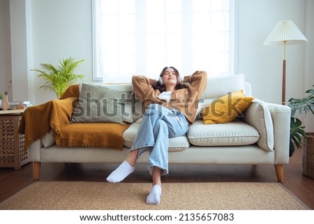 Beautiful young asian woman with headphones relaxing and listening to music on the sofa . relax and chill out concept. Royalty-Free Stock Photo #2135657083