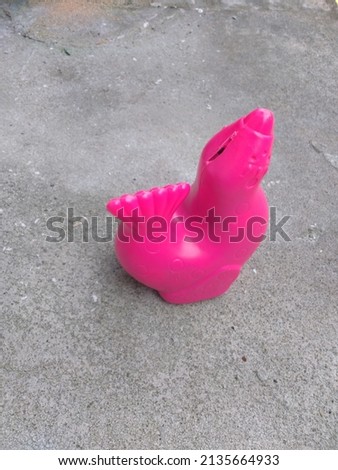 picture of chicken bank for kids with pink colour and full of coin inside, put on the floor on sunny day