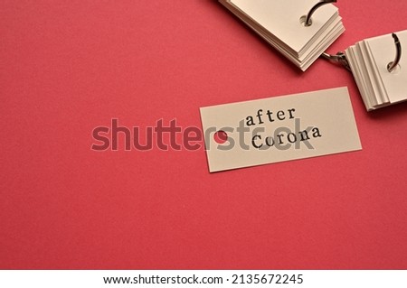 There is a small card placed on a red background paper with the word after Corona written on it. Copy space available.