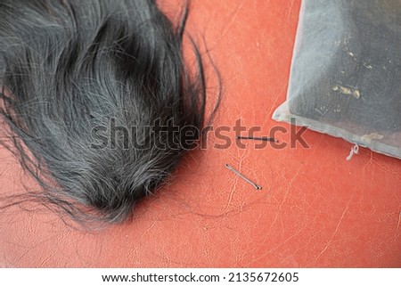 A black wig rests on an orange background with hairpins. Royalty-Free Stock Photo #2135672605