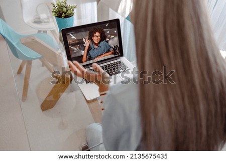 Close up of cheerful woman on notebook display showing ok gesture and smiling while female friend sitting at the table at home