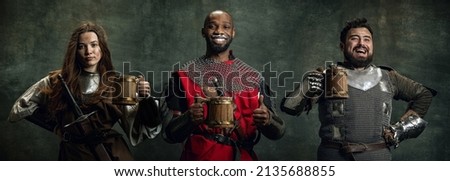 Beer festival. Creative collage with happy men and woman in image of medieval warriors holding big mugs of frothty beer, ale isolated over dark vintage background. Comparison of eras, renaissance Royalty-Free Stock Photo #2135688855