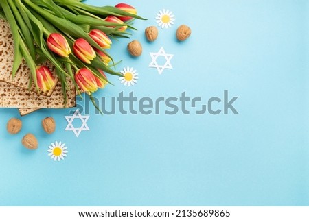 Jewish holiday Passover greeting card concept with matzah, nuts and tulip flowers on blue table. Seder Pesach spring holiday background, top view, copy space. Royalty-Free Stock Photo #2135689865