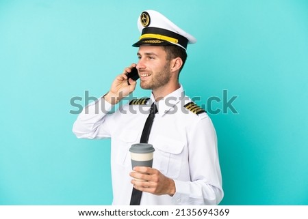 Airplane caucasian pilot isolated on blue background holding coffee to take away and a mobile