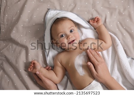 Mother applying moisturizing cream onto her little baby's skin on bed, closeup Royalty-Free Stock Photo #2135697523