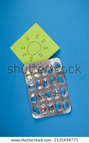 D Vitamin pills on blue backgroun, yellow stick note draw sun
