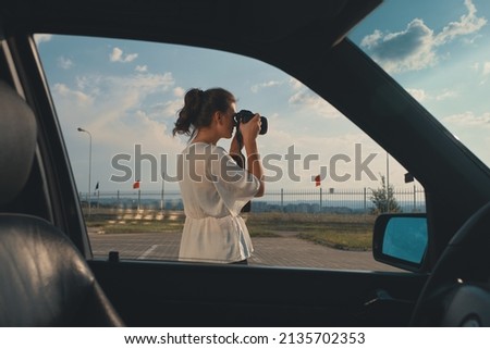 Female driver taking picture during her journey. Carefree lady has stopped in the parking lot to immortalize the amazing sky.