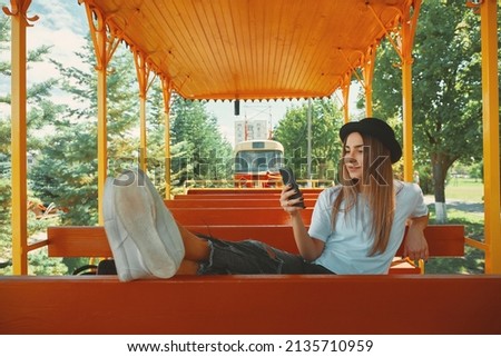 An attractive girl in her 20s takes pictures for her blog while travel with a tram in the background using a city tour transportation. Girl making selfie.