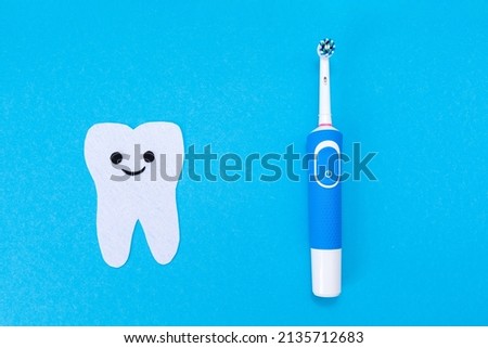 Electric toothbrush, toothpaste, a tooth carved out of felt with a smiling cartoon face. Blue background. Flat lay. The concept of dental care products.