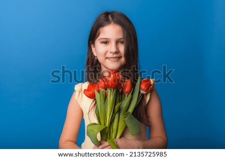 Little cute girl holding a bouquet of tulips on a blue background. Happy women's day. Place for text. Vivid emotions. March 8