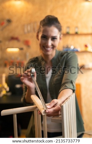 Portrait of woman carpenter measuring a wooden chair in workshop