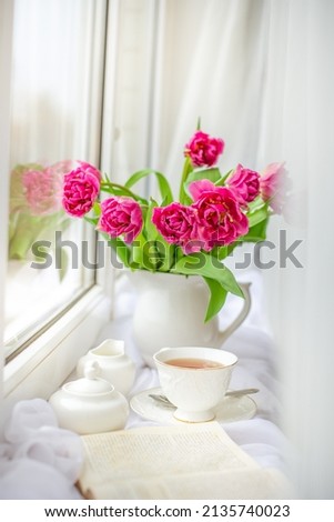 a spring still life, a bouquet of tulips in a vase, a cup of tea and an old book are lying on the window. spring greeting card with spring flowers