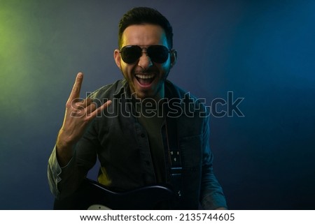 Handsome famous artist with black glasses making the rock sign and performing on a concert