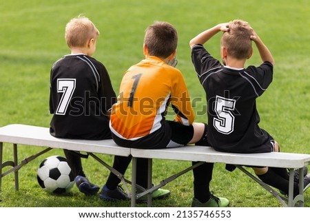 Soccer players sitting on sideline bench. School football team. Youth soccer players sitting together on substitute bench and watching match Royalty-Free Stock Photo #2135746553