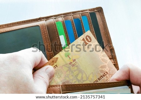 Man hand putting 10 Saudi riyal banknote in the wallet. 