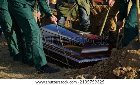 Burial. Men lower the coffin into the grave. n Royalty-Free Stock Photo #2135759325