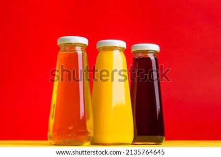 Bottles with yellow and red liquid halthy beverage on yellow and red background. Orange apple cherry