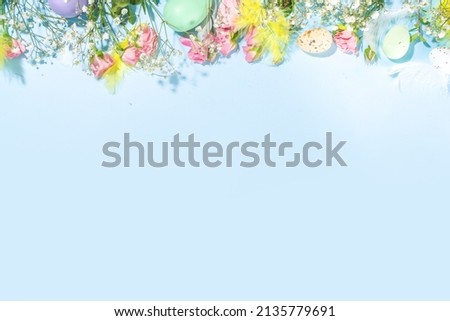Easter spring background with Easter eggs, colorful feathers, flowers and green leaves, high-colored bright sunny blue background, top view frame