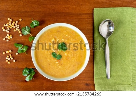 Yellow split peas lentil soup, garnished with corrinader leaves, in a bowl with a spoon and napkin on a wooden table. View from above. Royalty-Free Stock Photo #2135784265