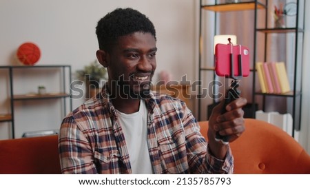 African American man blogger looks at device screen taking selfie on mobile cell phone cam, make virtual video call online on modern social media vlog application. Guy with smartphone on sofa at home