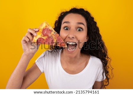 Closeup Portrait Of Excited Young Lady Enjoying Pizza Holding And Showing Slice Posing Over Yellow Orange Studio Background Wall. Junk Food Lover Eating Italian Pizza. Unhealthy Nutrition Cheat Meal Royalty-Free Stock Photo #2135794161