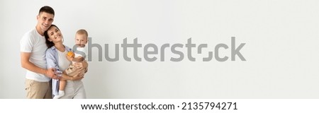 Happy Young Parents Holding Their Cute Toddler Son And Smiling At Camera, Portrait Of Beautiful Cheerful Family Of Three With Little Baby Posing Together Over White Background, Copy Space, Panorama