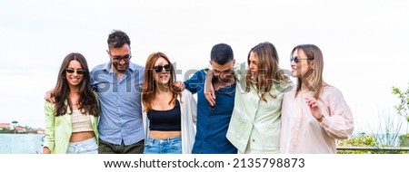 young people stroll embraced in a city park - Concept of friendship and happiness - Group of young friends walking - teenagers having fun together – student walk outside – horizontal banner or header 