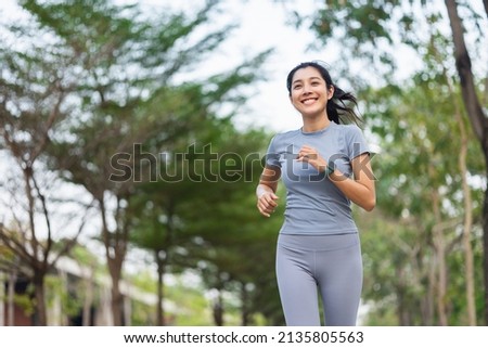 Happy slim woman wearing sportswear jogging in the city at sunrise. Young beautiful asian female in sports bra running outdoor. Workout exercise in the morning. Healthy and active lifestyle concept. Royalty-Free Stock Photo #2135805563