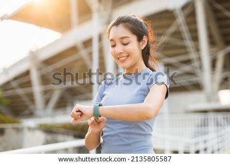 Woman checking sports smart watch in the city at sunrise. Asian female adjusting smart watch before workout outdoor. Exercise in the morning. Healthy and technology lifestyle concept.