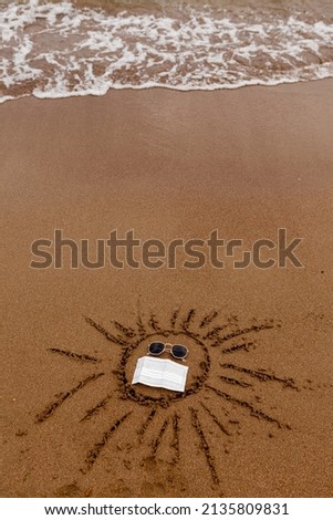 traveling during a pandemic. Mask as a necessary attribute for travel. A symbol of the sun painted on the sand wearing glasses and a medical mask. 