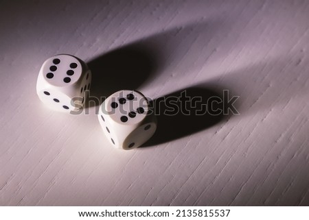 Details of gambling cubes on white wooden table, illuminated from aside, hard shadow details. 