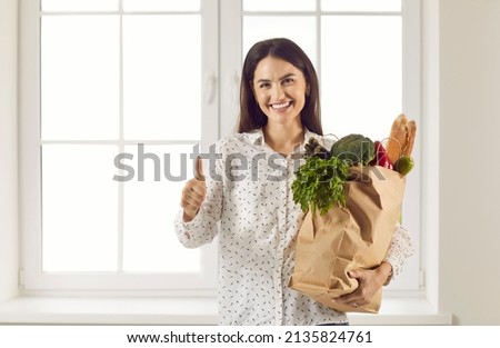 Happy woman with bag full of fresh foods rich in vitamins and good for cooking wholesome meal for family. Customer satisfied with quality of shopping and express delivery smiling and giving thumbs up