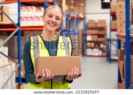 Portrait Of Female Worker Holding Box Inside Warehouse Royalty-Free Stock Photo #2135829697