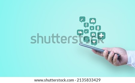 A hand holding a mobile phone with a speech bubble of healthcare and medical icon on a turquoise background with copy space.