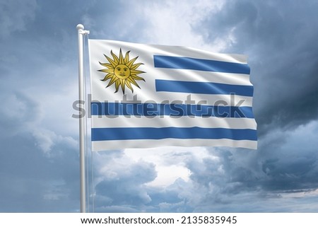 Uruguayan flag on a flagpole waving in the wind on a dramatic cloudy sky background. Flag of Uruguay
