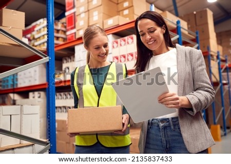 Female Team Leader With Clipboard In Warehouse Training Intern Standing By Shelves Royalty-Free Stock Photo #2135837433