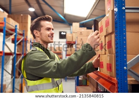 Male Worker Wearing Inside Warehouse Scanning Stock Barcode On Shelves Using Digital Device Or Phone Royalty-Free Stock Photo #2135840815