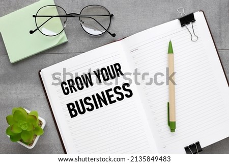 grow your business. gray background with open notepad with text. near glasses and plants