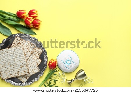 Composition with Passover Seder plate, flatbread matza and flowers on yellow background