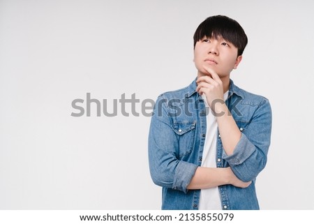 Pensive thoughtful young asian korean boy man student thinking about buying new clothes goods, opinion about sale offer discount isolated in white background Royalty-Free Stock Photo #2135855079