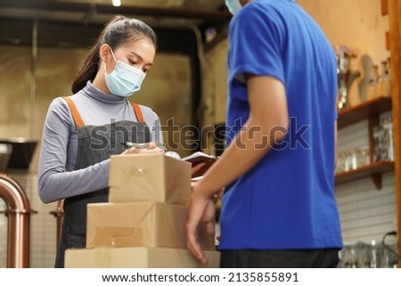 Waitress wearing mask check the box from food supply delivery man to restaurant pick up point and take away from online order as new normal while coronavirus or COVID-19 outbreak Royalty-Free Stock Photo #2135855891