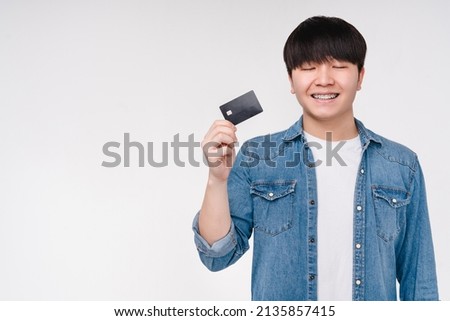 Asian korean young man boy student freelancer with eyes closed holding credit card making a wish for shopping buying new gadgets, loan cashback e-commerce isolated on white